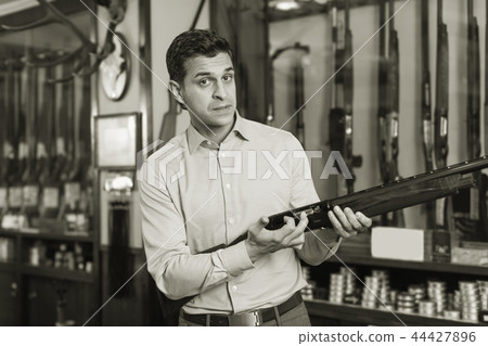 Adult male seller in hunting shop demonstrating shotgun 44427896