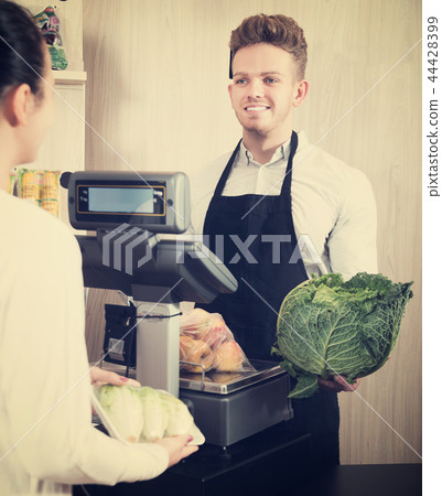 Seller assisting customer to weigh purchases Seller assisting customer to weigh purchases 44428399