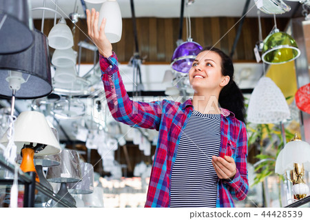 Girl in lighter shop chooses stylish and modern chandelier lamp Girl in lighter shop chooses stylish and modern chandelier lamp 44428539