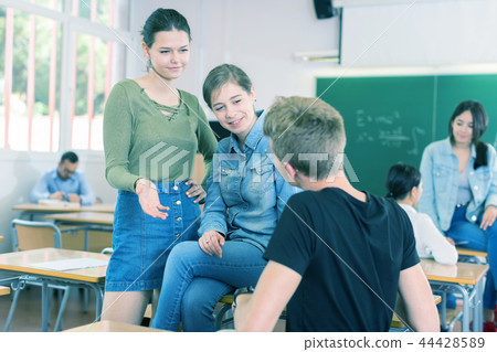 Smiling schoolgirls and boy are talking about homework at the desk 44428589