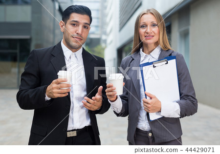 Businessman and his woman colleague in suit are standing with folder and coffee Businessman and his woman colleague in suit are standing with folder and coffee 44429071