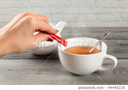 Detail on woman hand pouring sugar from small pack 44440228