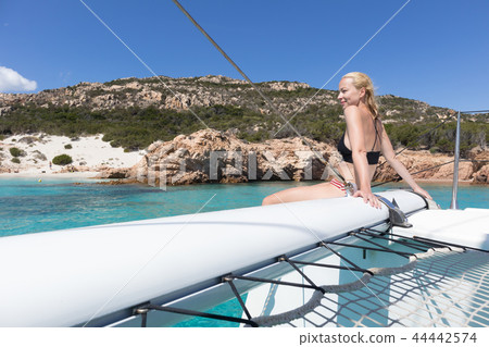 Woman relaxing on a summer sailing cruise, sitting on a luxury catamaran near picture perfect white Woman relaxing on a summer sailing cruise, sitting on a luxury catamaran near picture perfect white 44442574