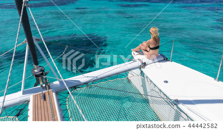 Woman relaxing on a summer sailing cruise, sitting on a luxury catamaran in picture perfect Woman relaxing on a summer sailing cruise, sitting on a luxury catamaran in picture perfect 44442582