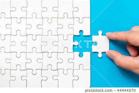 Hand putting piece of white jigsaw puzzle Hand putting piece of white jigsaw puzzle 44444870