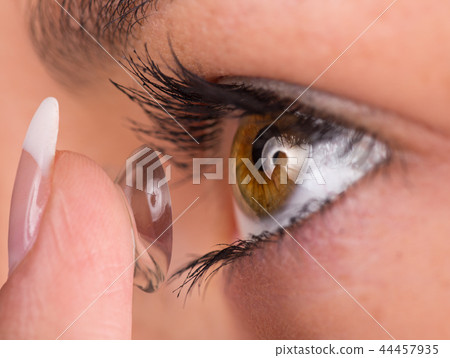 Young woman putting contact lens in her eye. Young woman putting contact lens in her eye. 44457935