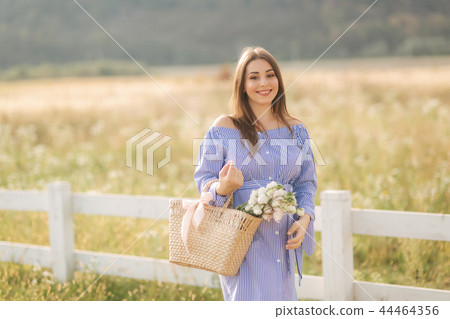 Close up view of beautiful pregnant woman in field holding bouquet and smile. Relax in nature 44464356