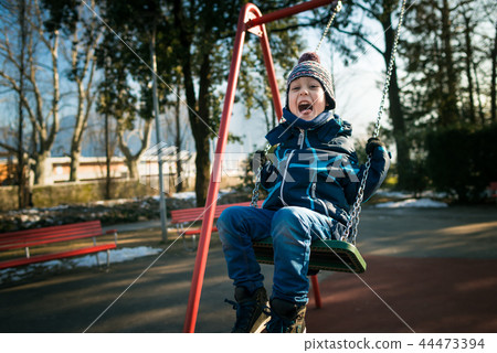 Happy little boy on swing in beautiful winter day Happy little boy on swing in beautiful winter day 44473394