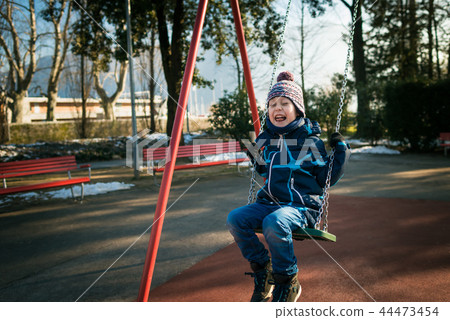Happy little boy on swing in beautiful winter day Happy little boy on swing in beautiful winter day 44473454