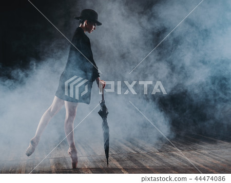 Ballerina in black long jacket and sexy bodysuit dancing on stage with magic light and smoke. Young Ballerina in black long jacket and sexy bodysuit dancing on stage with magic light and smoke. Young 44474086
