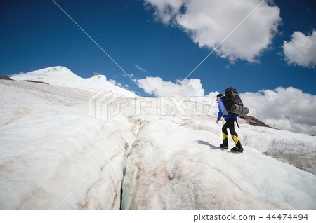 A mountaineer with a backpack walks in crampons walking along a dusty glacier with sidewalks in the A mountaineer with a backpack walks in crampons walking along a dusty glacier with sidewalks in the 44474494