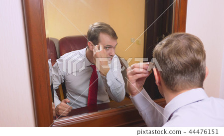 the concept of metrosexualism. a handsome man in front of a mirror takes care of his face. does the the concept of metrosexualism. a handsome man in front of a mirror takes care of his face. does the 44476151