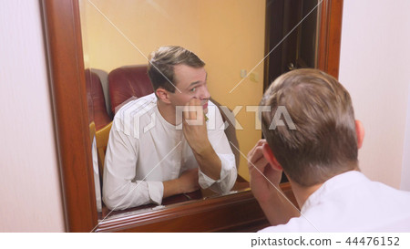 the concept of metrosexualism. a handsome man in front of a mirror takes care of his face. does the the concept of metrosexualism. a handsome man in front of a mirror takes care of his face. does the 44476152