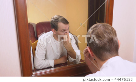 the concept of metrosexualism. a handsome man in front of a mirror takes care of his face. does the the concept of metrosexualism. a handsome man in front of a mirror takes care of his face. does the 44476153