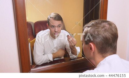 the concept of metrosexualism. a handsome man in front of a mirror takes care of his face. does the the concept of metrosexualism. a handsome man in front of a mirror takes care of his face. does the 44476155