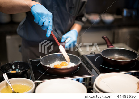 Hotel chef hands with gloves cooking fried eggs Hotel chef hands with gloves cooking fried eggs 44481650