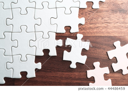 Plain jigsaw puzzle in the process of assembly. Wood grain background. Plain jigsaw puzzle in the process of assembly. Wood grain background. 44486459