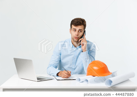 Confident architect. Handsome young man with hardhat and blueprint and talking on the mobile phone Confident architect. Handsome young man with hardhat and blueprint and talking on the mobile phone 44487880
