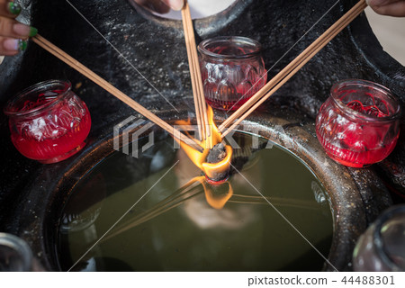 Three hand holding incense sticks over a burning candle 44488301