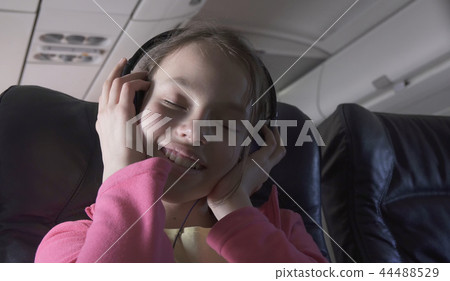 Cheerful teenage girl listens to music on headphones in the cabin of plane while traveling 44488529