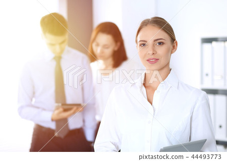 Beautiful blonde businesswoman standing straight in a brightly lit office at the background of Beautiful blonde businesswoman standing straight in a brightly lit office at the background of 44493773
