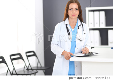 Doctor woman at work. Portrait of female physician filling up medical form while standing near Doctor woman at work. Portrait of female physician filling up medical form while standing near 44494147