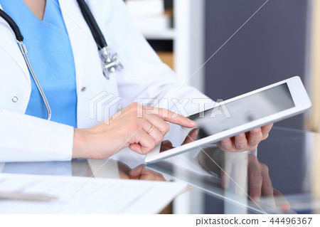 Woman doctor using tablet computer while standing straight in hospital office, closeup. Healthcare Woman doctor using tablet computer while standing straight in hospital office, closeup. Healthcare 44496367
