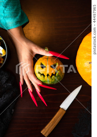 Image of woman's hands with pink nails with pumpkin jack, spider, knife sitting at wooden table 44497965