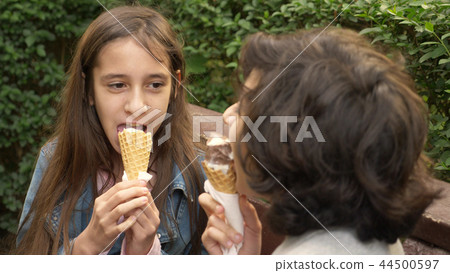 cute teenagers, boy and girl eating ice cream in the park and talking 44500597