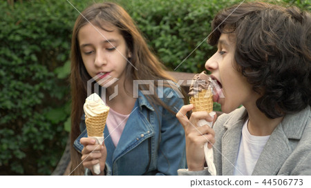 cute teenagers, boy and girl eating ice cream in the park and talking 44506773