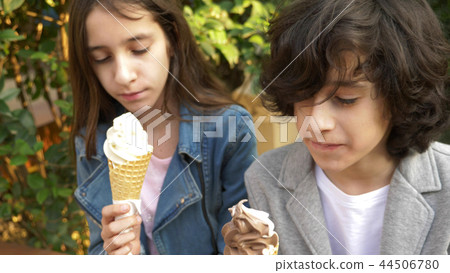 cute teenagers, boy and girl eating ice cream in the park and talking 44506780