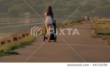 Beautiful young woman pushing stroller along waterfront pathway Beautiful young woman pushing stroller along waterfront pathway 44510399