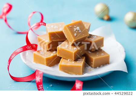 Caramel fudge candies on a plate with Christmas red ribbon on blue background. Close up. Caramel fudge candies on a plate with Christmas red ribbon on blue background. Close up. 44529022