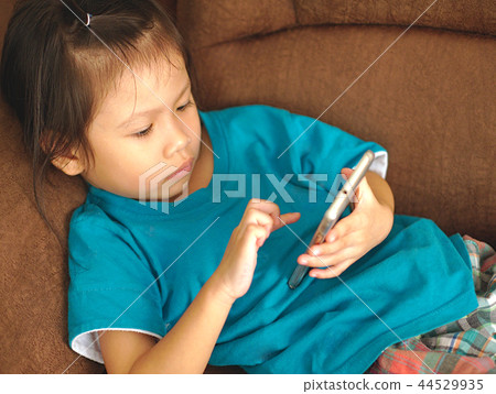 Little Asian kid using smartphone on sofa bed. Little Asian kid using smartphone on sofa bed. 44529935