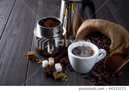 ground coffee is filled with a geyser coffee maker and cup of coffee wit spices on a wooden table on 44533215