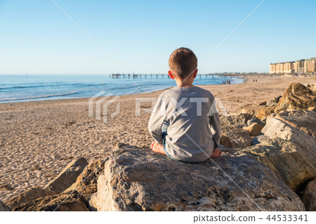 Lonely barefoot boy sitting on the rock 44533341