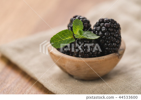 fresh blackberries in wood bowl on wooden table with mint leaves 44533600