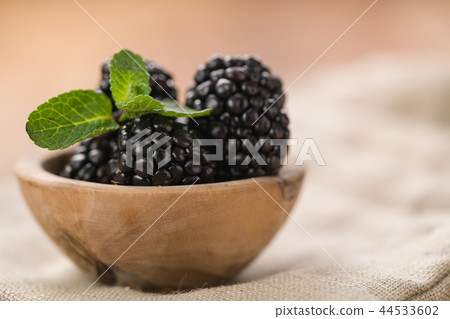 fresh blackberries in wood bowl on wooden table with mint leaves 44533602