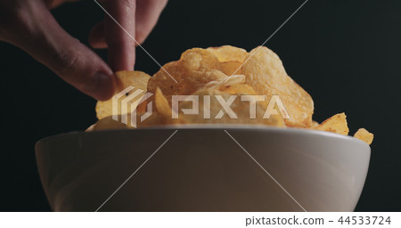 closeup man hand taking potato chip from white bowl low angle shot closeup man hand taking potato chip from white bowl low angle shot 44533724