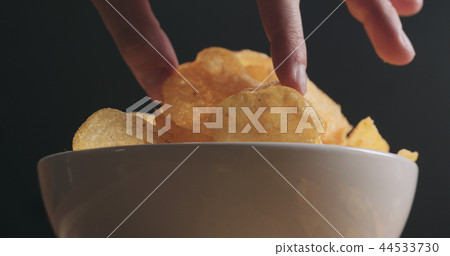 closeup man hand taking potato chip from white bowl low angle shot closeup man hand taking potato chip from white bowl low angle shot 44533730