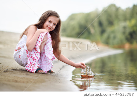 girl child playing with toy sailing ship by river girl child playing with toy sailing ship by river 44533797