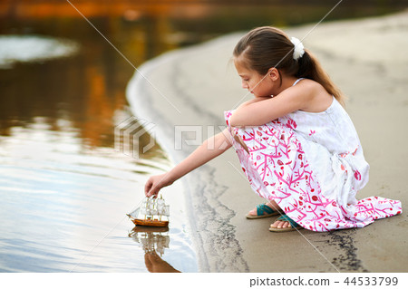 girl child playing with toy sailing ship by river girl child playing with toy sailing ship by river 44533799