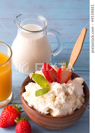 Fresh cottage cheese with strawberries in a wooden bowl with a spoon, glass of milk, jar of juice on Fresh cottage cheese with strawberries in a wooden bowl with a spoon, glass of milk, jar of juice on 44539881