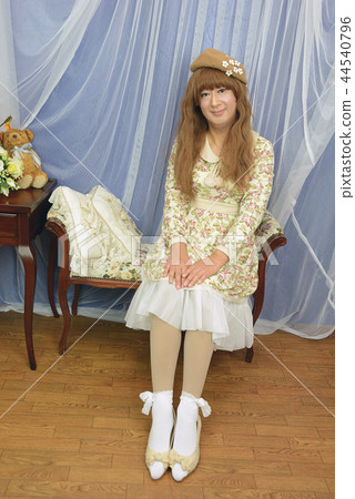 米色的花朵圖案連衣裙全身女人坐在椅子上戴著一頂帽子，把她的手放在膝蓋和微笑 44540796