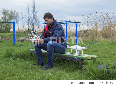 A man with a remote control quadroopter in his hands is sitting on a bench. White quadroopter A man with a remote control quadroopter in his hands is sitting on a bench. White quadroopter 44541939