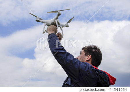 A man with a quadrocopter in his arms raised to the sky. A white drone is being prepared for the 44541964