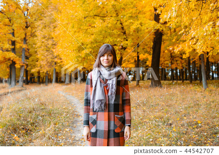 Portrait of young woman in fall forest. Brunette woman in autumn park with fashionable plaid coat 44542707