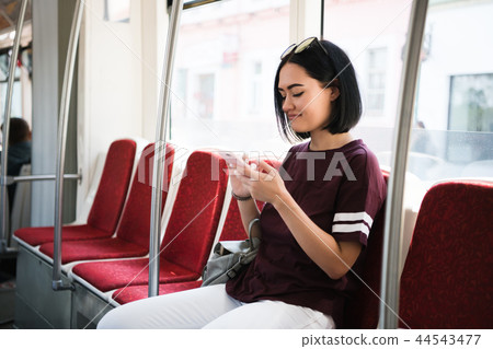 Young adorable joyful woman is sitting in the bus using the phone and smiling. Young adorable joyful woman is sitting in the bus using the phone and smiling. 44543477