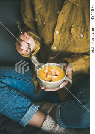 Woman sitting and eating warming pumpkin soup from mug 44544075
