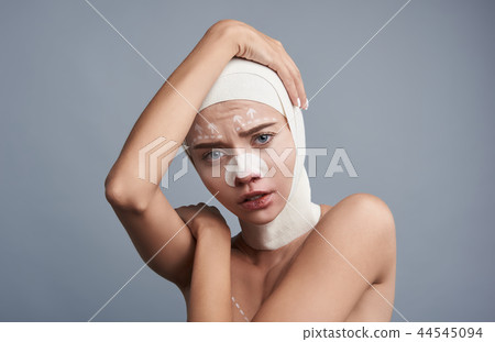 Sad lady touching her head while having bandages on it Sad lady touching her head while having bandages on it 44545094